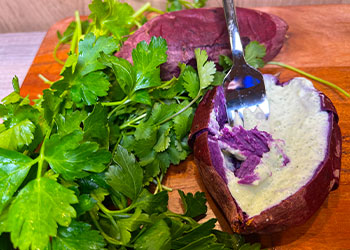 Baked Purple Sweet Potato with Herbed Yogurt with fork that shows the deep purple color balanced against a background of fresh parsley.