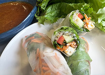 Spring rolls with crispy tofu are displayed on a white plate with sauce in a blue bowl and lettuce leaves in the background.