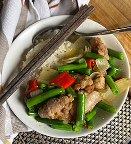 Vibrant colors of ginger green bean chicken stir-fry served on white plate with gray chopsticks.