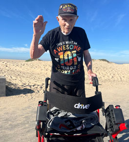 transcatheter valve replacement TAVR patient Joe bush walking on the beach with his wheelchair, wearing a black t shirt saying this is what an awesome 101 year old looks like
