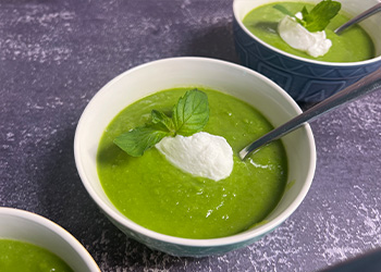 Three bowls of Spring Pea Soup with Mint displayed on purple textured counter.