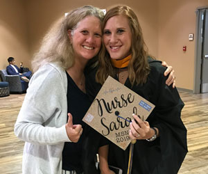 uci health nurses amy dobson and sarah martinez standing together smiling at sarah's graduation indoors while sarah holds a graduation cap saying nurse sarah and amy gives a thumbs up