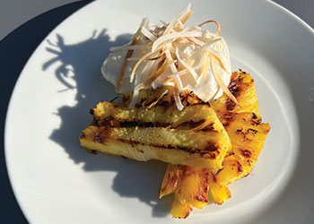 Hawaiian grilled pineapple with whipped coconut yogurt basked in sunlight on a white plate.