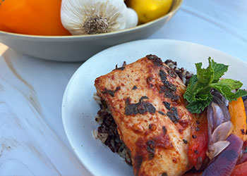 Aleppo pepper mahi-mahi with mint served on rice in a white bowl with fresh pepper, garlic and lemons in the background.