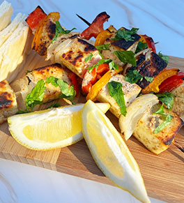 Chaat masala-spiced paneer and vegetables skewers are arrayed on a white plate with a side of rice and lemon wedges.