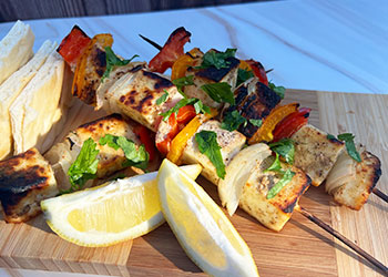 Chaat masala-spiced paneer and vegetables skewers are arrayed on a white plate with a side of rice and lemon wedges.