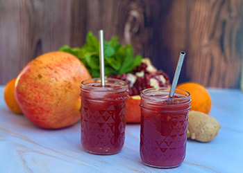 Two sunshine pomegranate mocktails sit on a marble top with fresh fruits in the background.