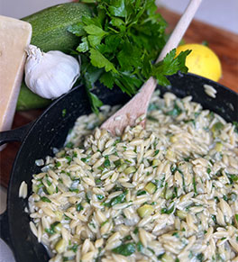 Lemony orzo with zucchini and parmesan served in a cast iron skillet with wooden spoon and fresh veggies in the background.
