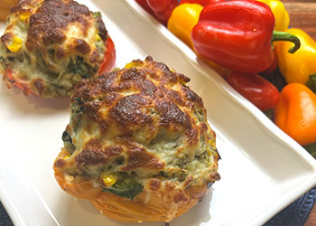 Two pesto chicken stuffed peppers sit on a white rectangle serving dish with multi-colored fresh peppers on the side.