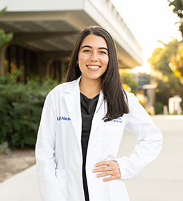 Carla Vazquez Vergara stands smiling in her UC Irvine School of Medicine white coat.