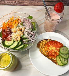 The salad, kimchi salmon met and strawberry kefir displayed together on a marble countertop.