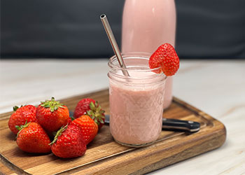 A mason jar filled with strawberry kefir sits on a wood cutting board with fresh strawberries and a glass bottle of kefir.