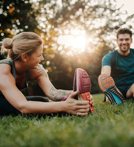 a man and a woman sit in the grass and stretch after exercising after a thanksgiving dinner