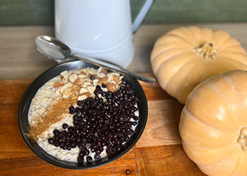 Creamy blueberry oatmeal bowl with almonds is served in black bowl with fresh mini-pumpkins and white pitcher on the side.