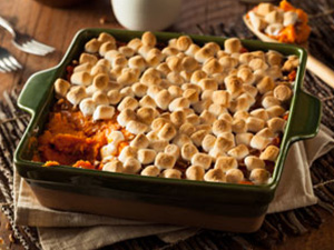 Scrumptious sweet potato casserole is served in a dark green square baking dish stacked atop wood cutting boards.