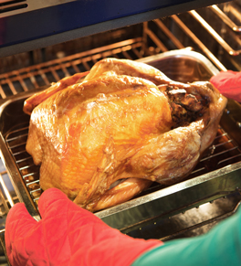 A browned turkey is being taken out of the oven by a person wearing protective gloves