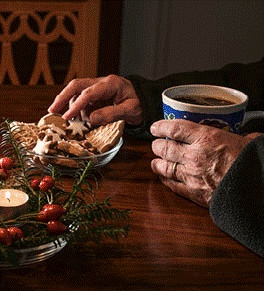 Closeup of an older adult holding a mug and taking a holiday cookie from a plate.