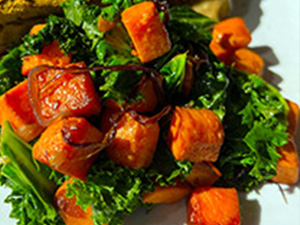 Kale and sweet potato stir-fry provides a colorful contrast on a white dish.
