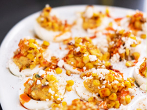 A dozen Mexican corn deviled eggs served with a drizzle of hot sauce.