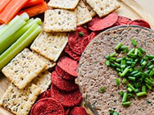 A bowl of mushroom lentil pate is served with a variety of crackers and crudite.
