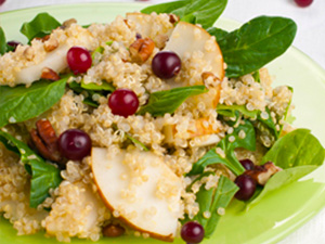 Refreshing pear and quinoa salad is served on a light green plate and garnished with cranberries.