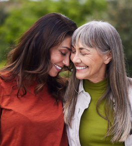 two women smiling with their heads together while standing outside