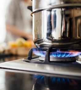 a steel pot on top of a gas stove that is lit with a person chopping food in the background the first week of february is burn awareness week