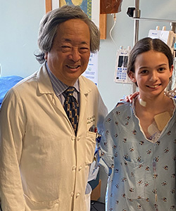 A smiling Dr. David Imagawa and Lauren Torres stand together in her hospital room after successful surgery.