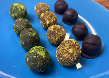 A variety of matcha and black bean chocolate truffles are displayed diagonally in three rows on a bright blue plate.