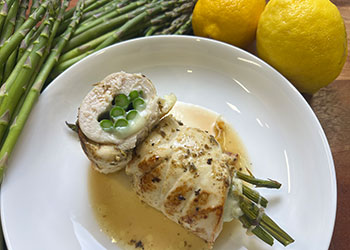 An overhead view of a chicken asparagus bundle with garlic sauce cut in half to show the asparagus and cheese filling.