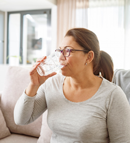 a hispanic woman preparing for her colonoscopy by drinking a glass of preparation in her living room