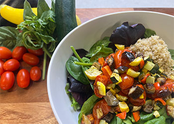 Roasted ratatouille salad with quinoa and balsamic reduction served in a white bowl.