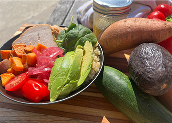 Roast turkey and sweet potato bowl is served in black bowl with fresh veggies all around it.