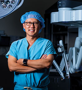UCI Health prostate cancer specialist Dr. David I. Lee stands near a robot-assisted surgery console in an operating room.