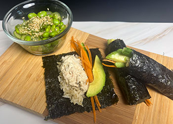 Two salmon nori avocado rolls are served with a side of cucumber edamame salad on bamboo cutting board.