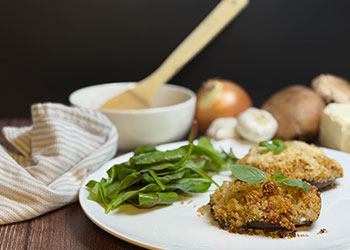 Two stuffed Portobello mushrooms are served with a mixed green salad on a white plate with ingredients in the background.