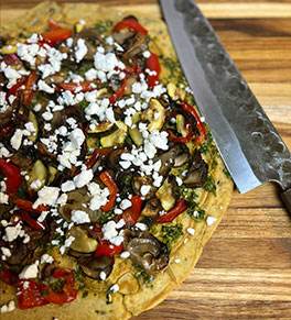 Vibrant and flavorful socca with roasted vegetables and chermoula is displayed on a wood cutting board.