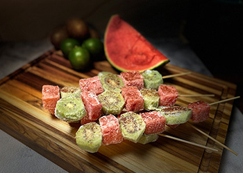 A pile of frozen watermelon kiwi skewers are washed in a bright light with a dark background.