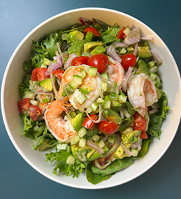 Refreshing shrimp and avocado salad is served in a white bowl on a blue counter.