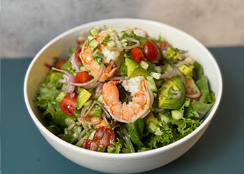 A big white bowl of shrimp and avocado salad sits on a blue countertop.