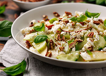 Apple, celery and toasted pecan salad in a white bowl sits on a grey placemat.
