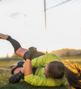 a young woman playing soccer falls to the ground with her legs in the air and gets a concussion