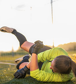 a young woman playing soccer falls to the ground with her legs in the air and gets a concussion