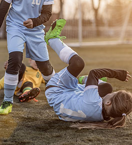 Soccer players gather around young player who has fallen and hit her head.