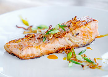 Pan-seared salmon drizzled with apple cider vinegar glaze is displayed on a white plate.