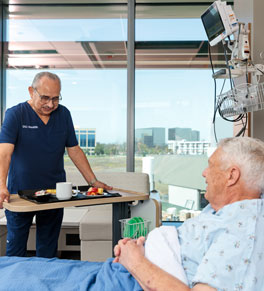 a nurse brings a patient nutritious food while he lays in bed under a blue blanket in one of the patient rooms at uci health — irvine