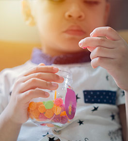 A four-year-old Asian boy holds a jar of gummy vitamins and contemplates whether to eat the one in his hand.