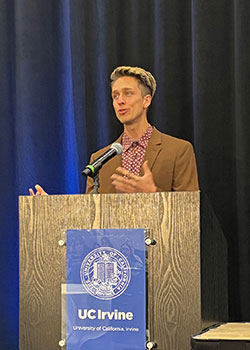 Living kidney donor Clayton Moore stands at a podium with a blue UC Irvine banner displayed in front.