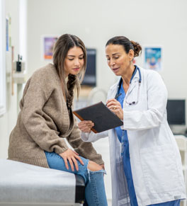 young asian woman dressed casually leaning over to look at something her doctor, wearing a white coat, is showing her