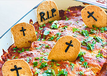 Pumpkin enchilada graveyard is served in a glass casserole dish with corn chip gravestones on top.
